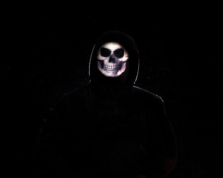 Person wearing a skull mask and black clothes against a black background.