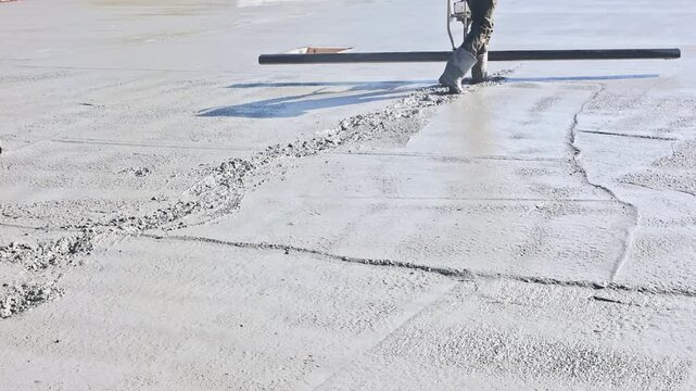 Concrete surface leveled, smoothed during construction with long straight edge tool