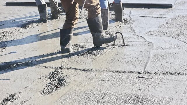 Worker in boots levels fresh concrete on construction site ground