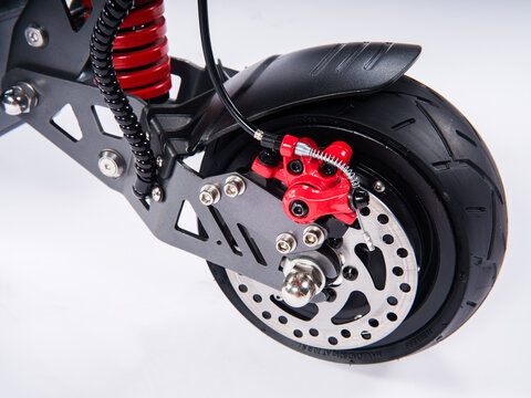 Close-up of electric scooter rear wheel with red disc brake caliper, tubeless tire and suspension on white background