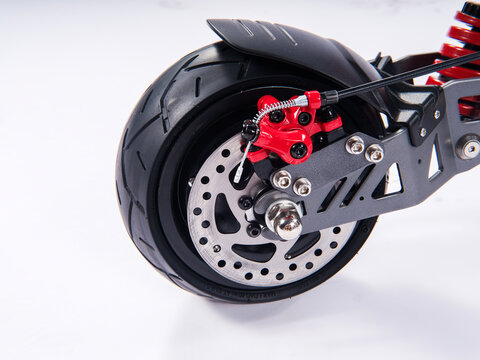 Close-up of electric scooter rear wheel with red disc brake caliper, tubeless tire and suspension on white background