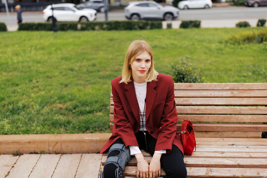 Young Person Sitting on a Bench in a Park With a Red Bag