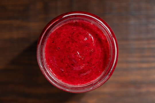 Red berry jam in glass jar top view, closeup. Fresh healthy red cranberry puree or fruit jam in glass jar, macro shot on dark wooden background