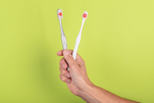 Hand holding two toothbrushes  on a green background