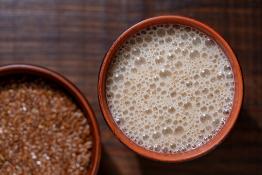 Flaxseed smoothie or plant milk with froth top view, closeup. Healthy vegan beverage with rich foam in ceramic cup next to brown flax seeds on dark wooden background, macro shot