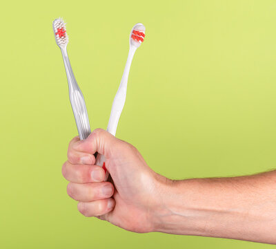Hand holding two toothbrushes  on a green background
