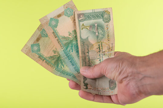 Hand holding dirhams banknotes of United Arab Emirates on yellow background