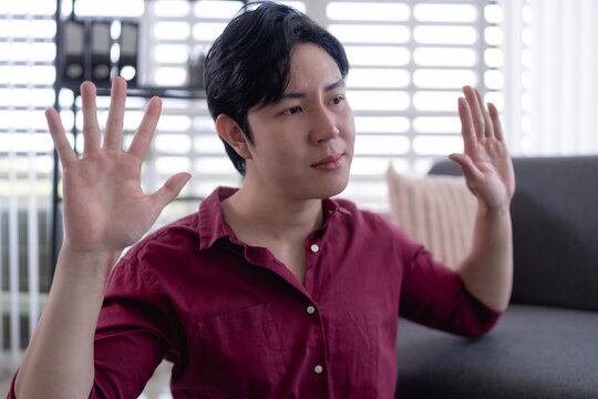 Young Asian man using hand gestures to communicate while sitting in bright modern living room