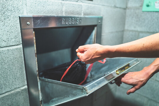 Woman Pushing a Trash Bag into a Rubbish Chute in an Apartment Building