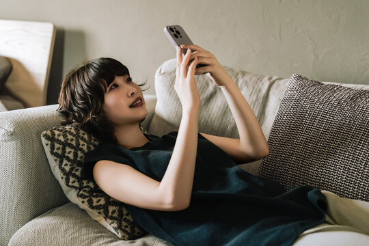 ソファに寝転んでスマートフォンを使う女性