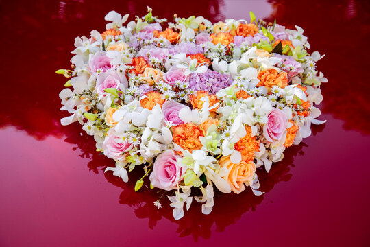 Round floral centerpiece with roses, orchids and carnations on glossy red reflective surface