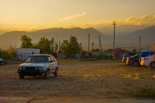 Rural Kyrgyzstani Landscape at Sunset with Parked Cars and Mountains