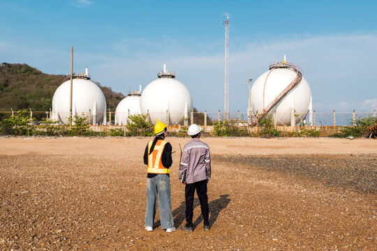 Two industrial workers inspect spherical storage tanks outdoors