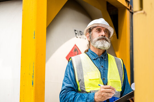 Bearded construction worker writing at an industrial site