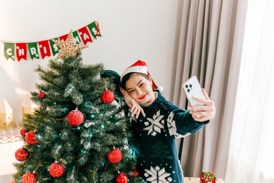 Woman in a Santa hat takes a selfie beside a Christmas tree