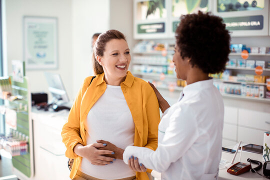 Pharmacist advising a smiling pregnant woman in a pharmacy