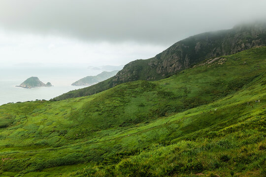 Misty coastal green hills with rocky islets and hikers