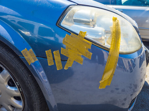 Close-up of blue car with yellow tape repair on fender and headlight