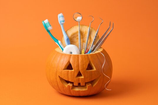 Halloween jack-o-lantern pumpkin filled with toothbrushes, dental floss and dental instruments on orange background