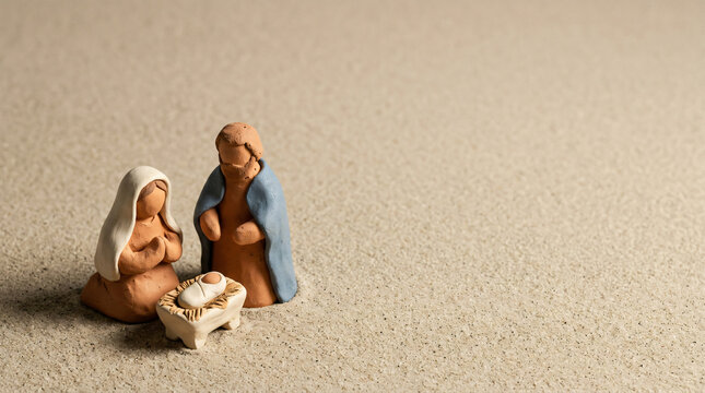 Terracotta nativity figure set gathered on a sandy surface. Minimalist Christmas holy family scene with copy space.