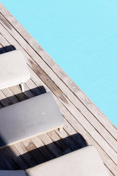 Wooden deck holding three cushions beside turquoise water while shadows stretching across planks