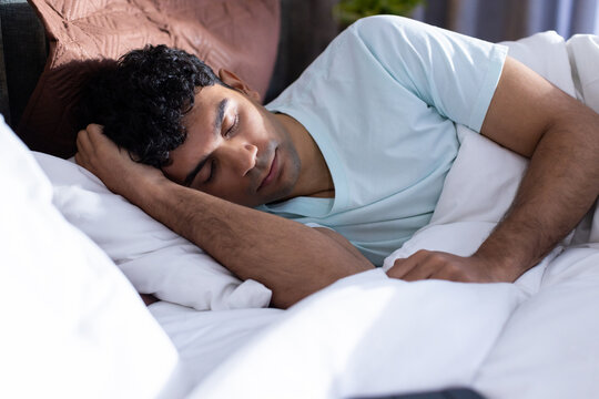 African American man sleeping on bed resting head on pillow near brown headboard in blue t-shirt