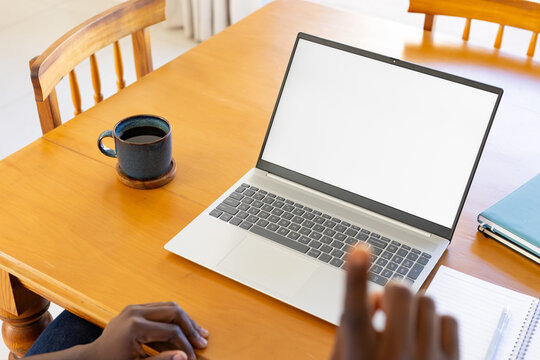 African American man sitting at wooden table with open laptop beside dark mug and notebooks