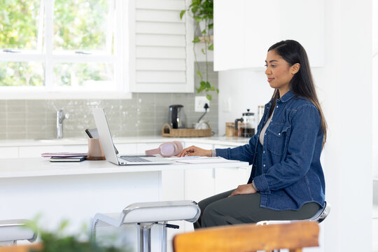 African American woman sitting at white kitchen island and typing on silver laptop