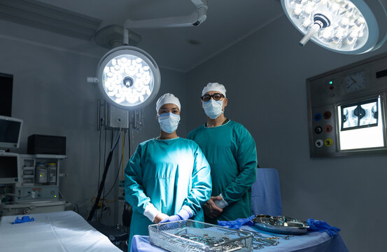 Diverse medical colleagues in teal scrubs standing behind draped table in operating room