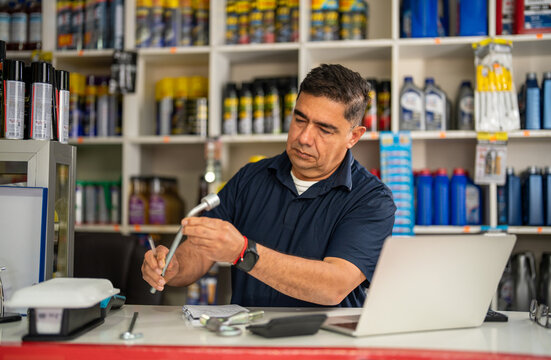 Automotive shop owner examining a metal car component beside a laptop in a parts store