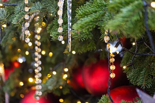 Pine branches with crystal beads and red baubles. Warm golden bokeh lights. Christmas tree decoration close-up. Background for New Year's or Christmas greetings. New Year's background for greetings