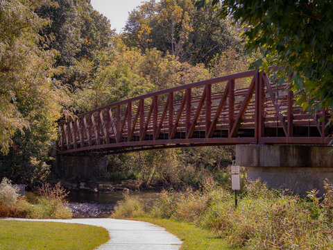 Pedestrian metal truss bridge crossing over river along scenic park pathway surrounded by autumn trees and nature