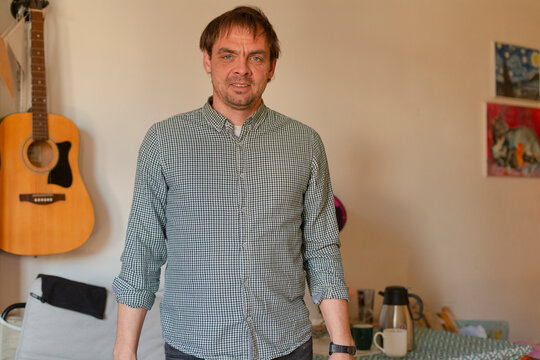 Man standing indoors wearing checked shirt with guitar in background