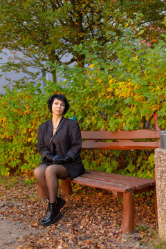 Woman in black blazer and gloves seated on wooden bench outdoors