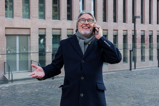 hispanic senior businessman talking on phone in a call outdoors in city, mature or elderly man using cellphone in cityscape 