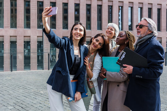 diverse business group of people taking a photo selfie together in a winter morning outdoors at cityscape. Successful Entrepreneurs multigenerational and multiracial teamwork using phone in city