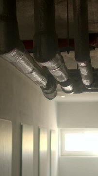 Insulated metal pipes and ductwork running along concrete ceiling of