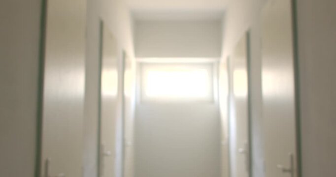 Narrow institutional corridor with closed doors and bright window at