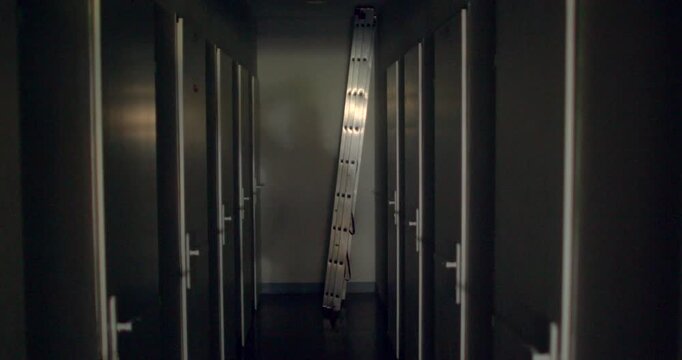 Narrow locker corridor with leaning aluminum ladder and vertical light