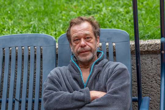 Serious middle aged man sitting outdoors with arms crossed and staring