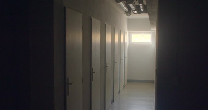 Dim school corridor with row of closed classroom doors and window back