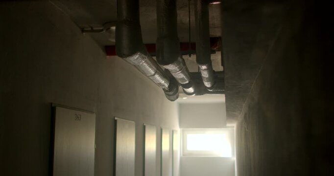 Exposed insulated pipes along ceiling in dim residential corridor with