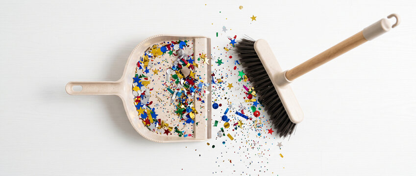 Broom and dustpan sweeping colorful confetti on a white background, post-party cleanup, festive mess and household cleaning concept