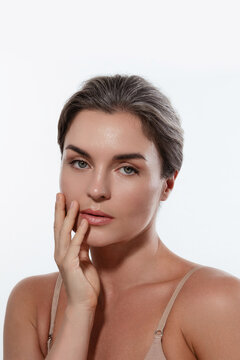 Beauty portrait of a woman with radiant skin, subtle makeup posing against a white background.