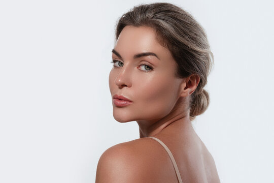 Beauty portrait of a woman with radiant skin, subtle makeup posing against a white background.