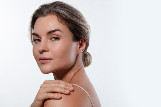 Beauty portrait of a woman with radiant skin, subtle makeup posing against a white background.