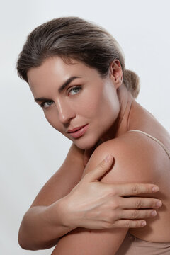 Beauty portrait of a woman with radiant skin, subtle makeup posing against a white background.