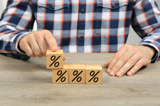 Man with wooden cubes at table, closeup. Blocks with percent signs. Discount concept