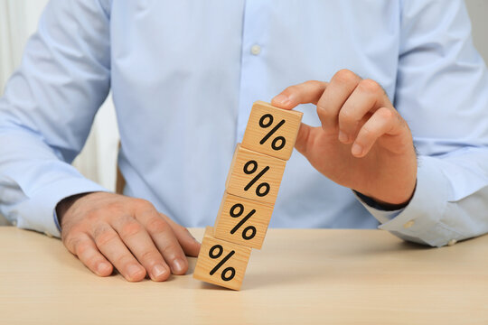 Discount concept. Man holding up tower of wooden cubes with percent signs to keep it from falling at table, closeup