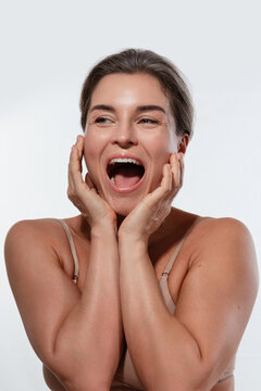 Excited Happy Woman with Glowing Skin Laughing with Mouth Open and Hands on Cheeks